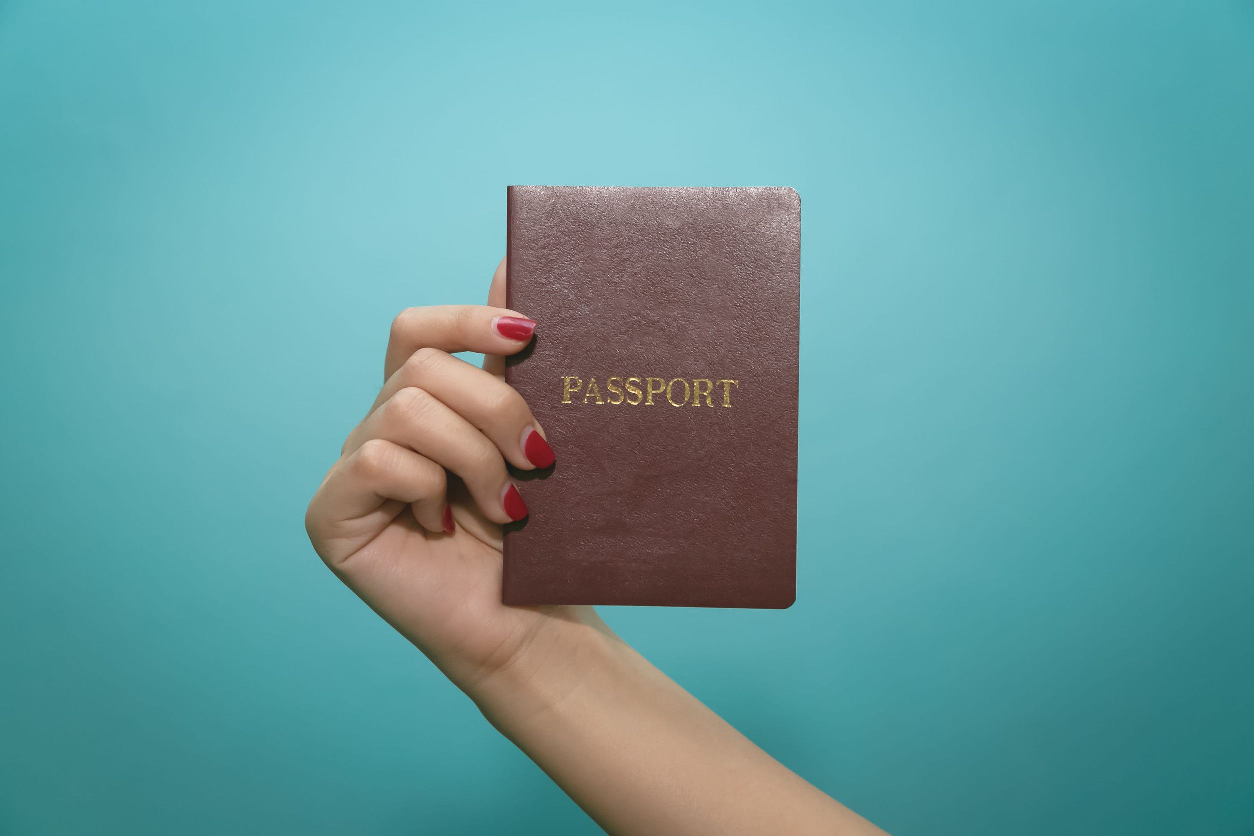 Hand Holding a Passport on Blue Background