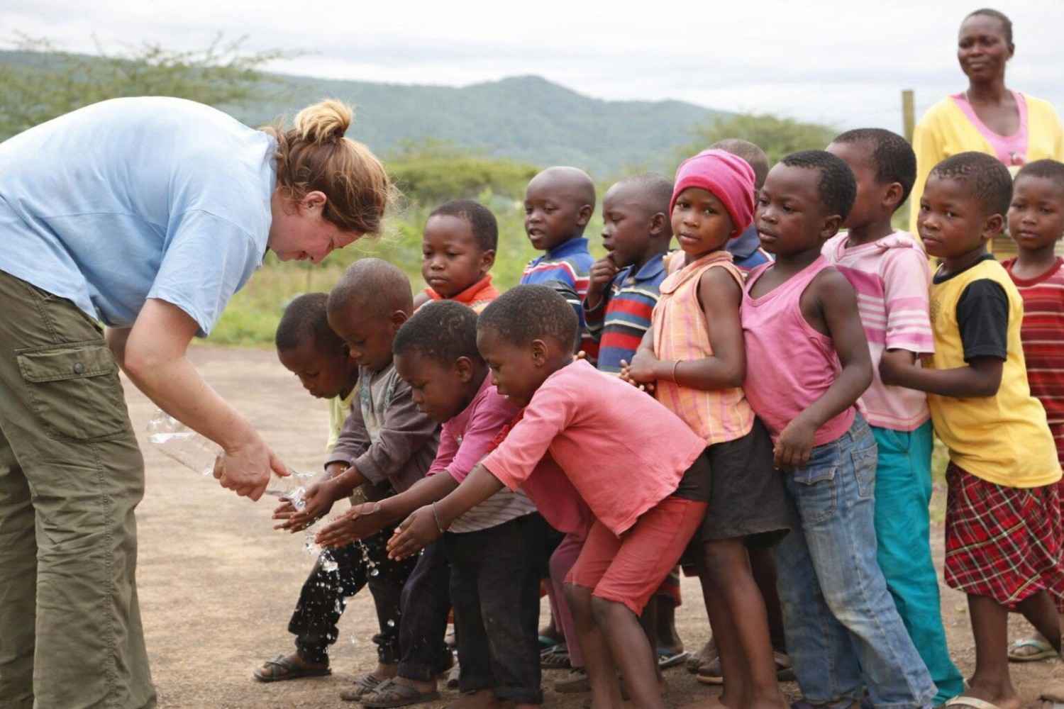 Volunteer Helping Children Wash Hands Outdoors
