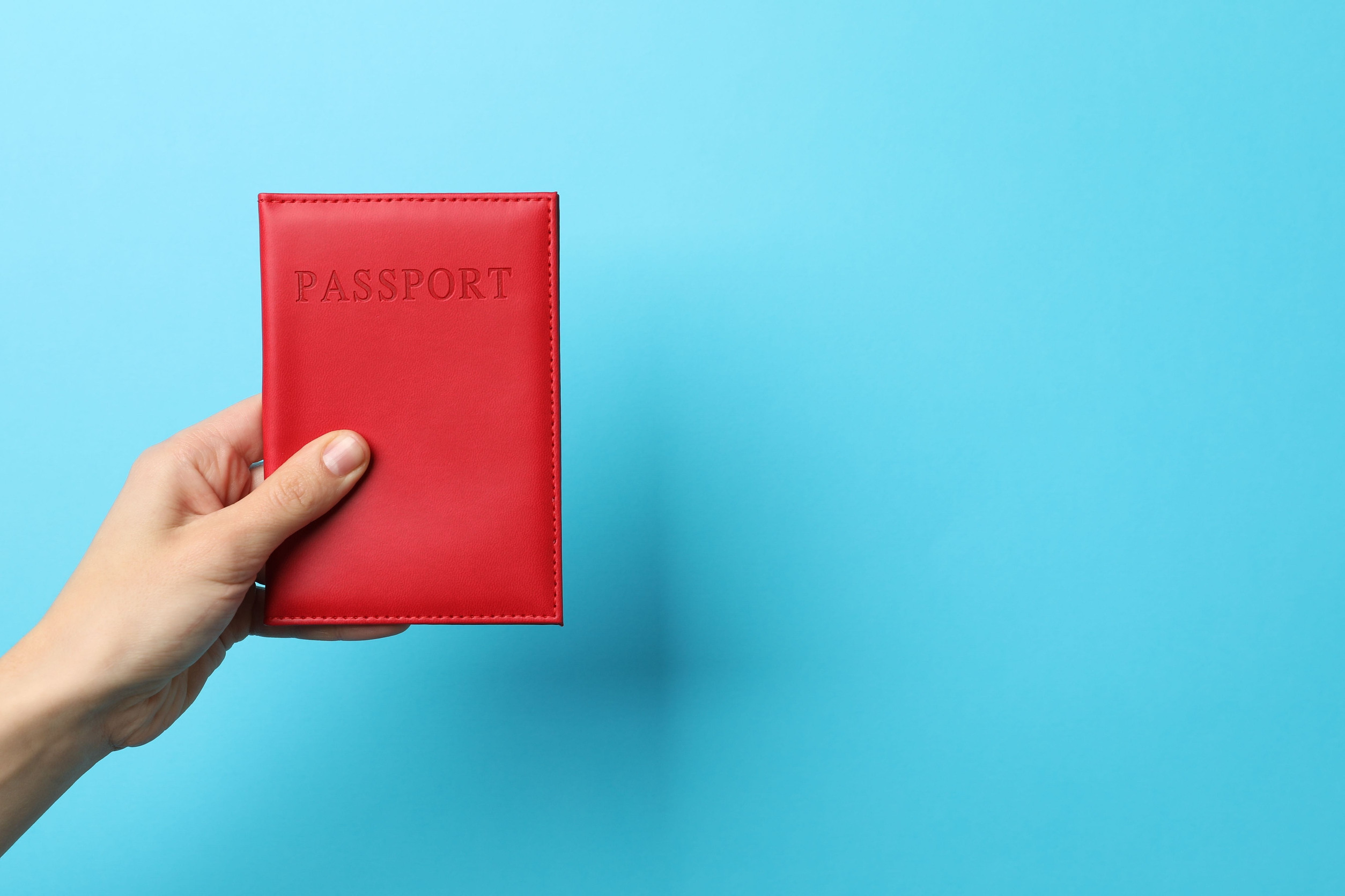 Woman Holding Passport in Bright Cover on Light Blue Background